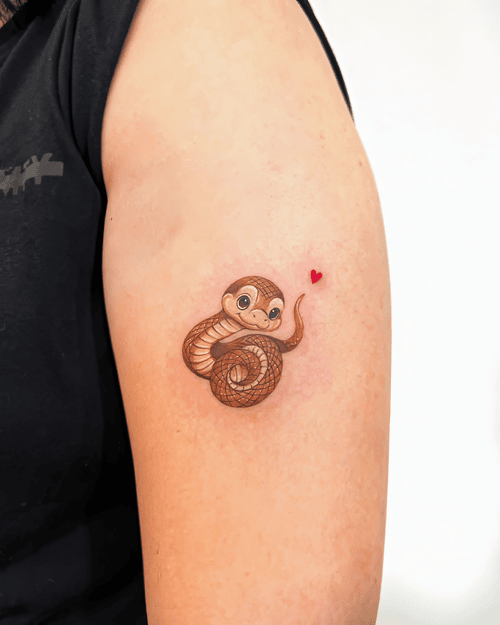 Xăm hình rắn chibi, mini tattoo dễ thương, xăm cánh tay màu nâu, heart accent tattoo: Em rắn chibi cuộn tròn kèm trái tim đỏ xinh xắn, điểm nhấn đáng yêu trên bắp tay.
